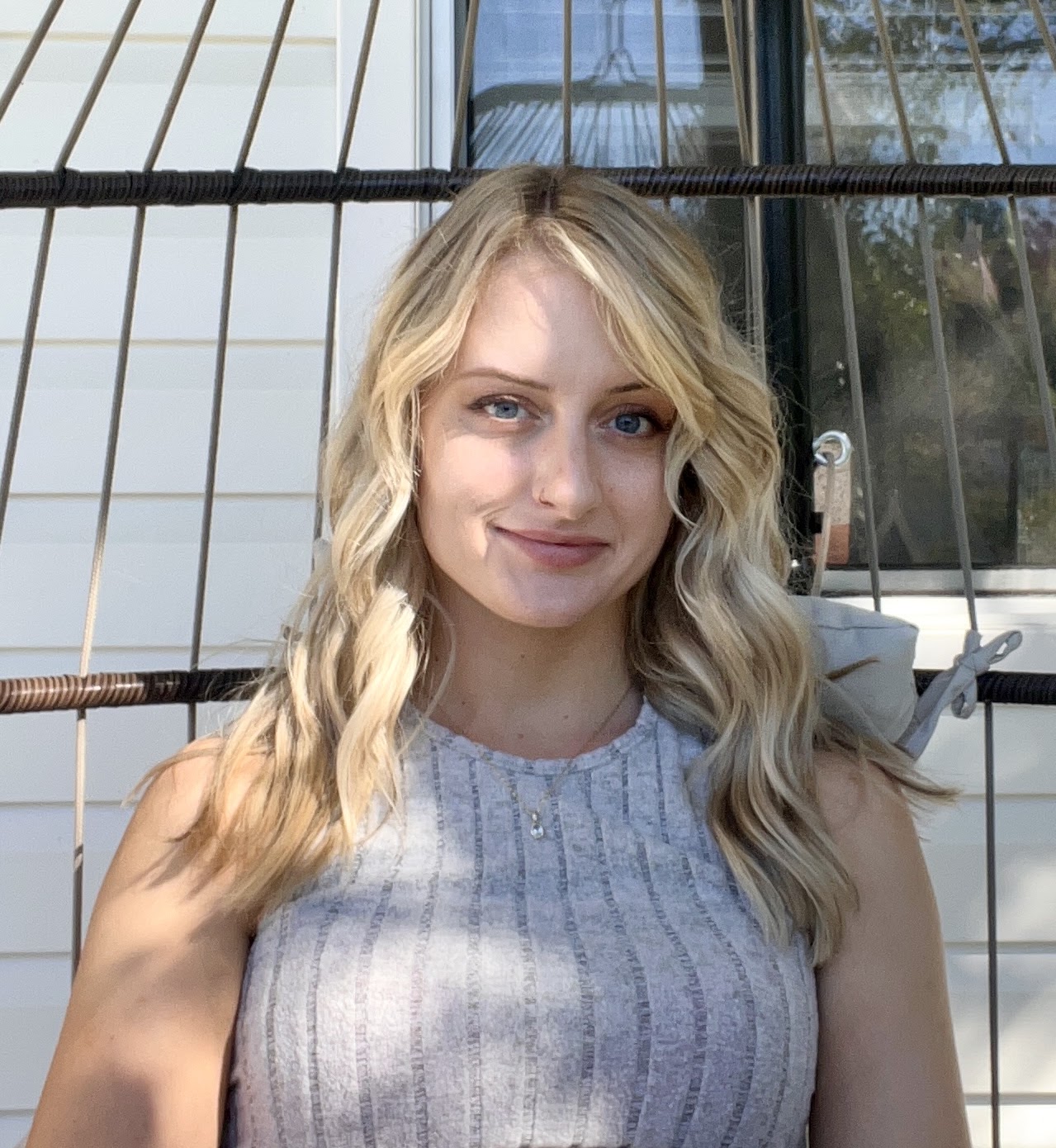 Portrait of a blonde woman sitting in an outdoor hanging chair.